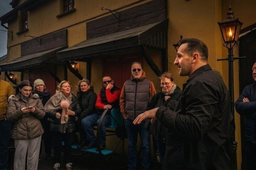 A group of people standing outside a building with a wooden facade and a lantern post. 1