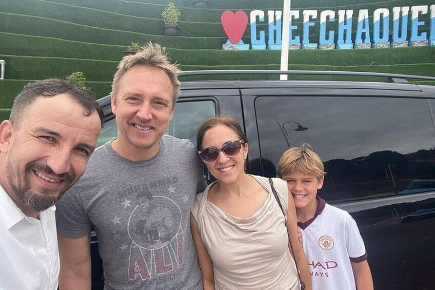 Una familia de cuatro personas posando frente a un vehículo negro con un letrero que dice 'CHEECHAOUE' al fondo. 1