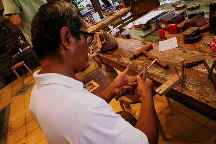 A person working at a wooden table with tools and materials, possibly in a workshop or craft area. 1