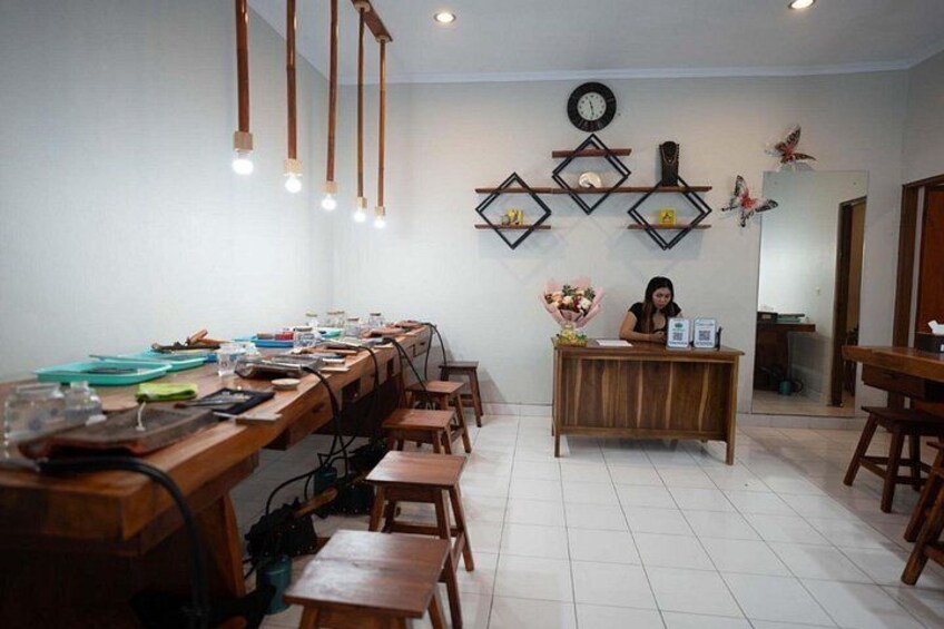 A conference room with a long wooden table, chairs, a desk with a person seated, and wall decorations including a clock and geometric shapes. 2