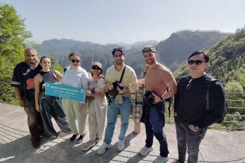 A group of people standing on a viewing platform with a mountainous landscape in the background. 1
