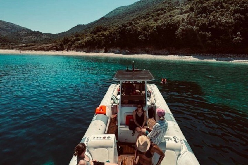 A boat on clear turquoise water with a beach and hills in the background. 1