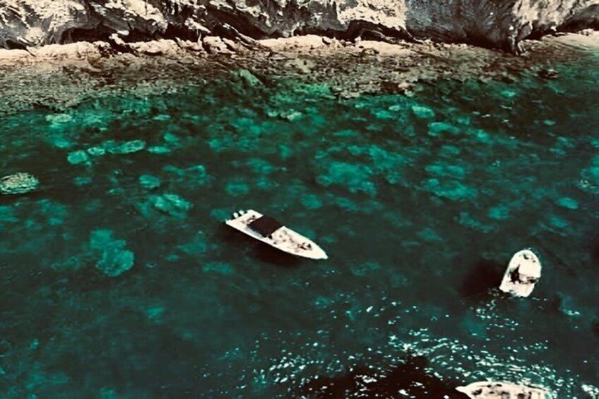 A boat on clear turquoise water with rocky cliffs in the background. 4