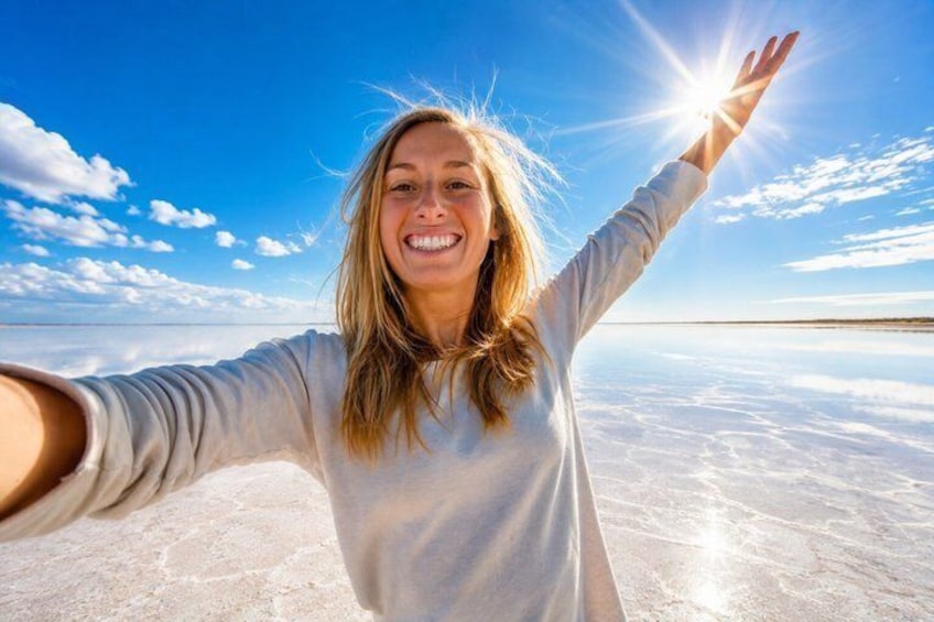 A person standing with arms outstretched on a flat, expansive salt flat under a clear sky. 1