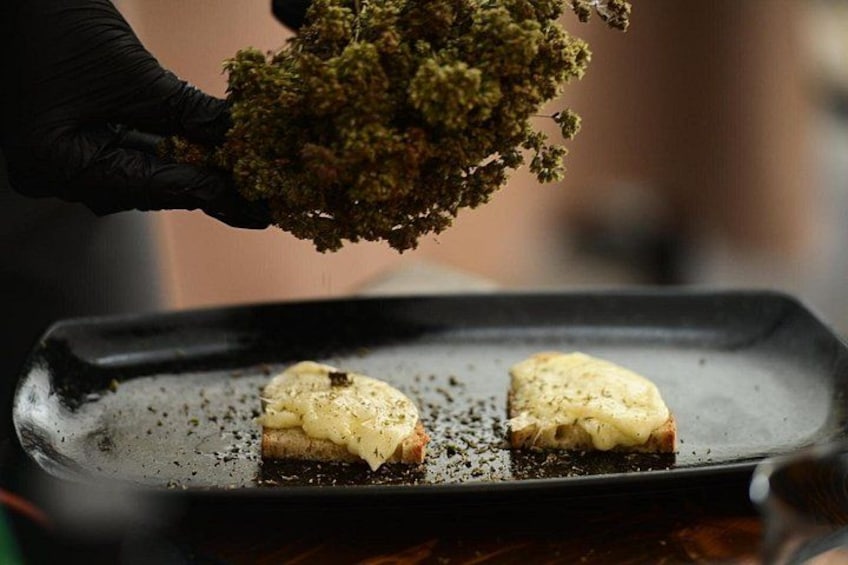 A person holding a sprig of greenery over a baking tray with two pieces of food. 3