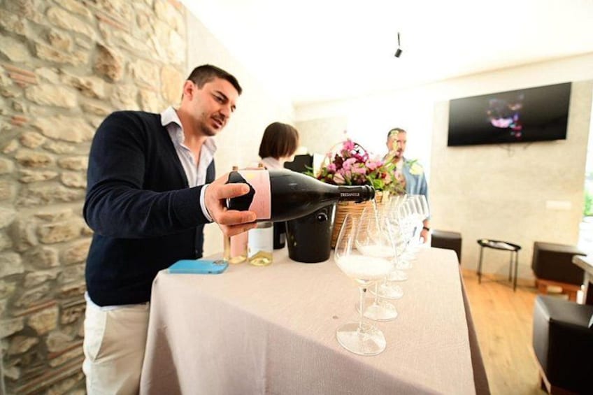 A person pouring wine into glasses on a table with a stone wall and a TV in the background. 4