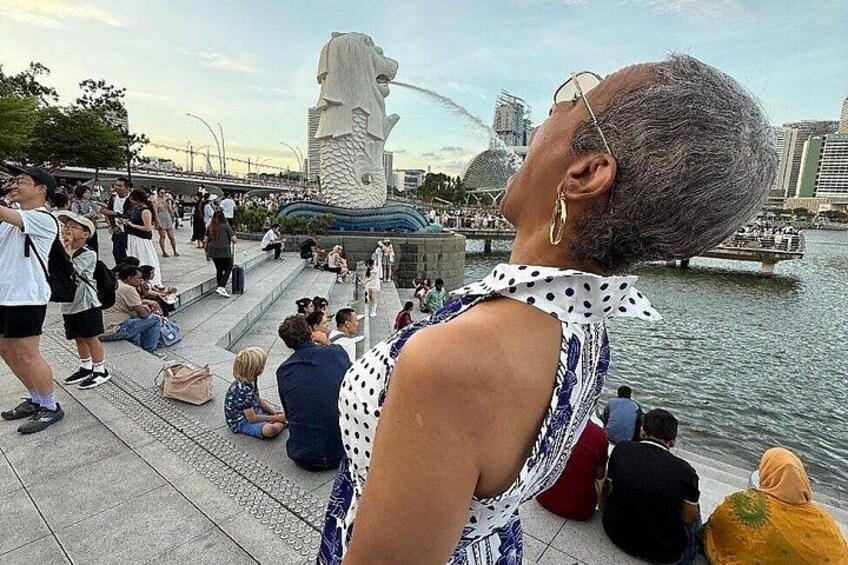 Guest posing playfully at Merlion Park Singapore with the iconic fountain in the background — part of the Omnicity Tours Singapore River Cruise & Night Tour. 3