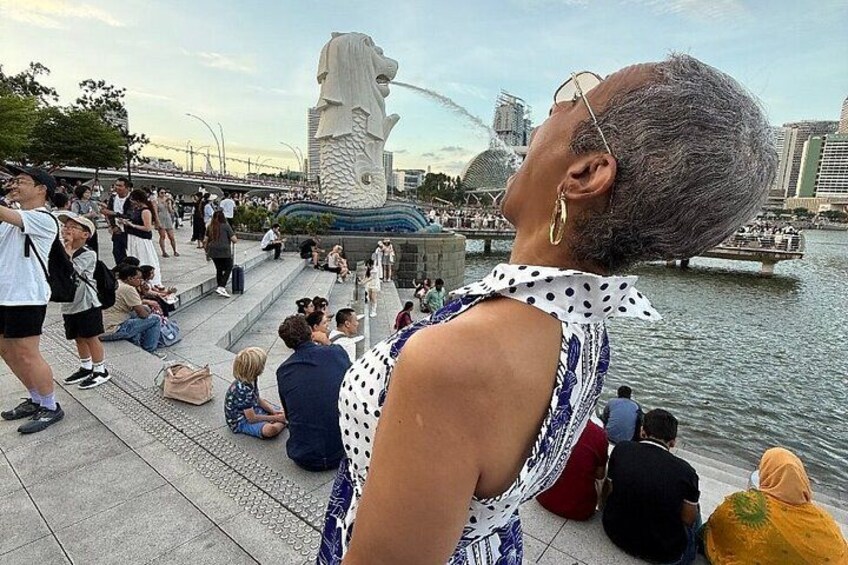 Guest posing playfully at Merlion Park Singapore with the iconic fountain in the background — part of the Omnicity Tours Singapore River Cruise & Night Tour. 2