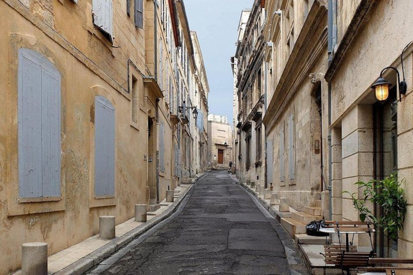 A narrow street flanked by old buildings with shutters, a cobblestone road, and a bench on the right. 4