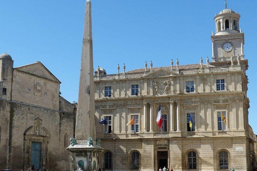 A historic building with a clock tower, a tall obelisk, and multiple flags. 3