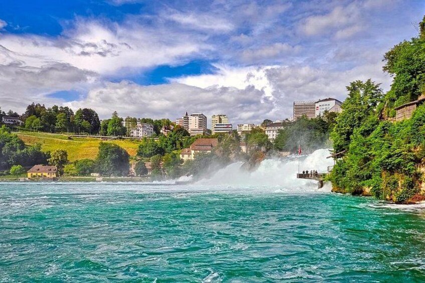 A coastal town with a waterfall, clear turquoise water, and buildings on the hillside. 2