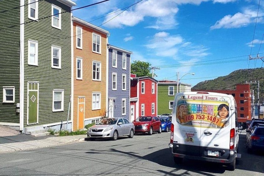 A street with colorful buildings, a white van with a travel advertisement, and parked cars. 3