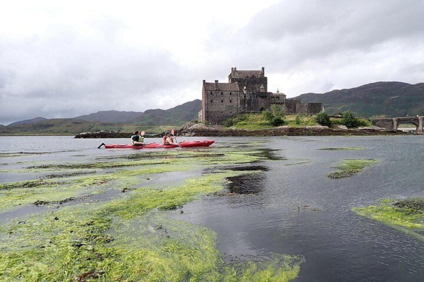 A castle on a hill, a red canoe on a calm body of water, and a bridge in the background. 1