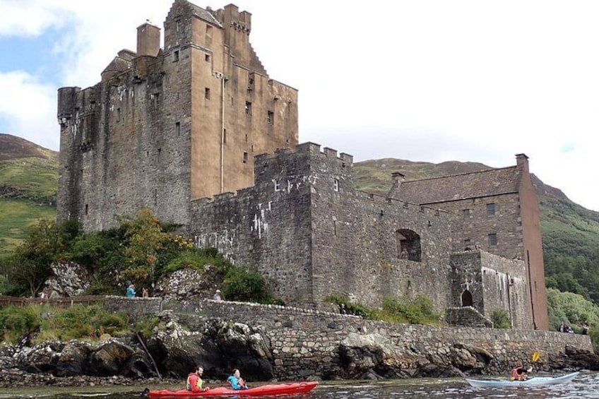 A historic castle by a river with people kayaking nearby. 4