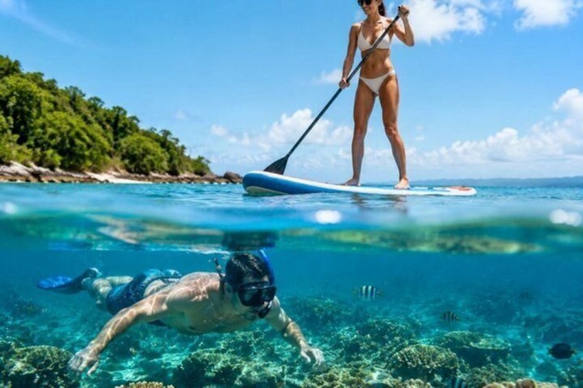 Une personne fait de la planche à pagaie sur une mer bleue et limpide, avec une île boisée en arrière-plan. 4