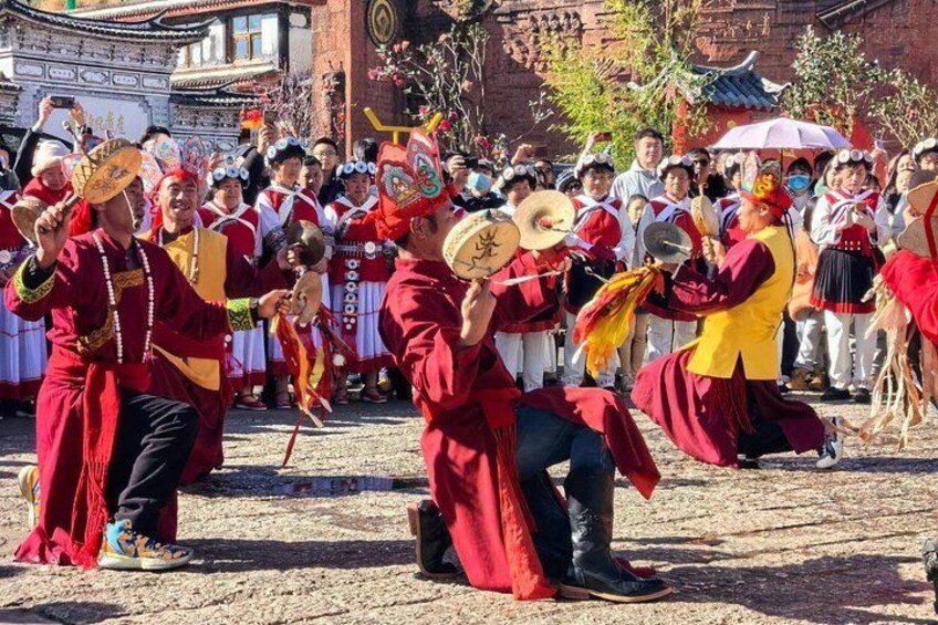 A group of people in traditional attire performing a dance with fans and props in an outdoor setting with buildings in the background. 5