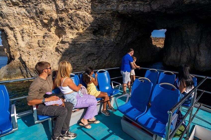 A boat tour with people seated on blue chairs, a rocky cliff in the background, and a clear sky. 5