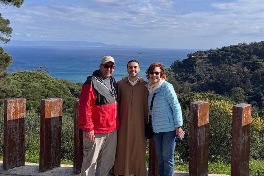 Trois personnes se tiennent sur une plateforme en bois, d’où l’on peut admirer un paysage magnifique sur l’océan et les collines qui se dressent à l’arrière-plan. 1