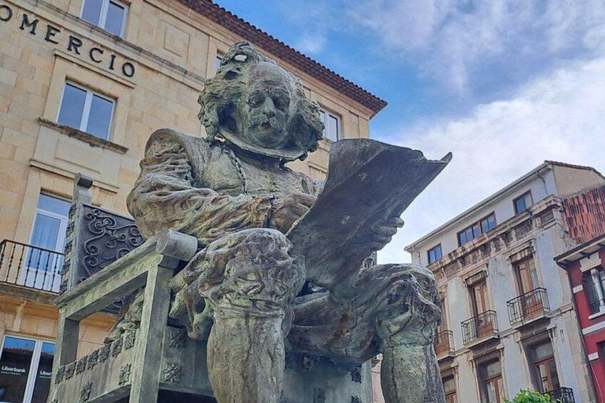 A bronze statue of a man with wings, set against a backdrop of buildings with balconies and a clear sky. 2