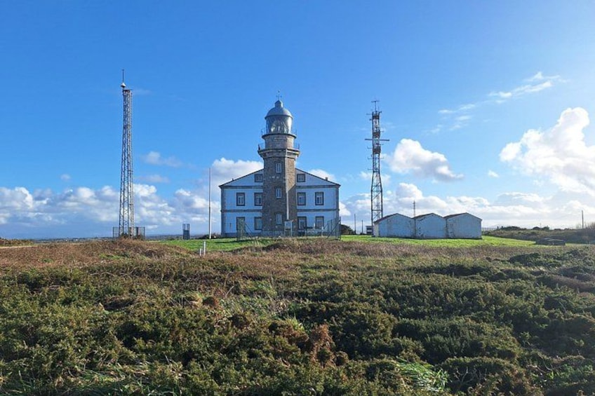 A lighthouse with a white facade, a tower, and two communication towers in a grassy landscape. 5