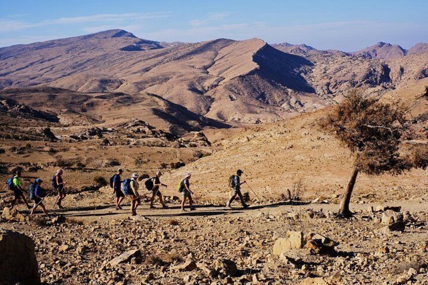 A group of hikers on a rocky trail with mountains in the background. 1