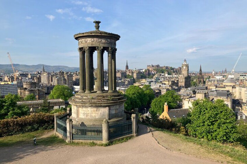 A historical monument with columns, surrounded by greenery, with a cityscape in the background. 2