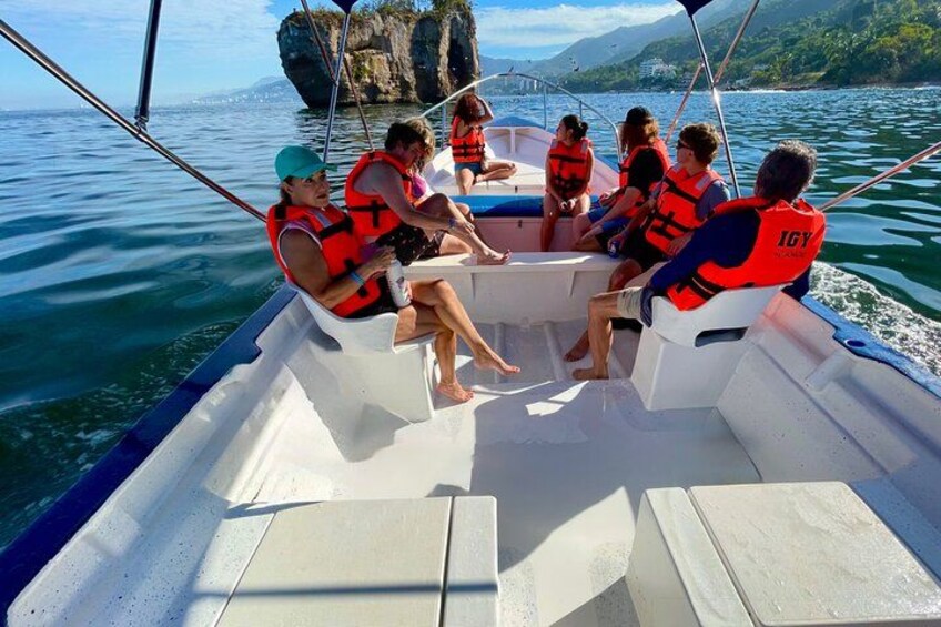 Un groupe de personnes à bord d’un bateau, portant des gilets de sauvetage, avec des falaises rocheuses et un ciel dégagé en arrière-plan. 2
