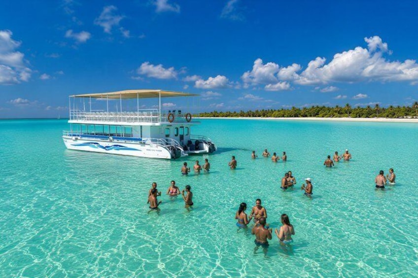 A boat with people swimming in clear turquoise water, a beach, and a line of palm trees in the background. 4