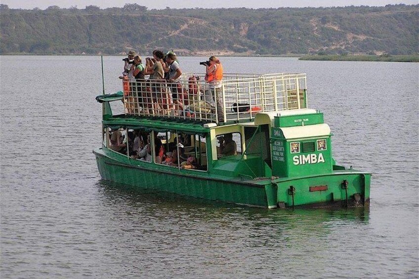 A green boat with the name 'SIMBA' on the front, carrying passengers on a calm lake. 1