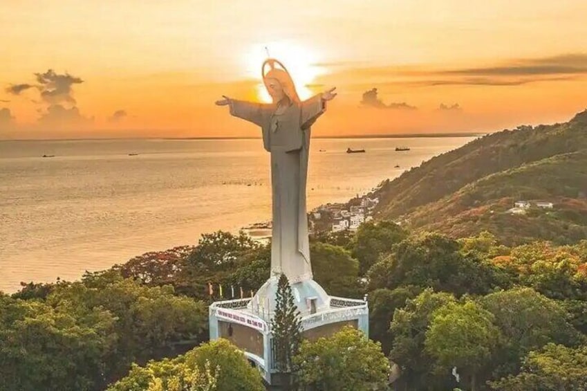 A statue of a figure with arms outstretched, overlooking a coastal landscape with trees and a body of water. 2