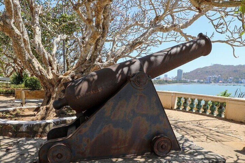 A cannon mounted on a pedestal, surrounded by trees and a body of water in the background. 1