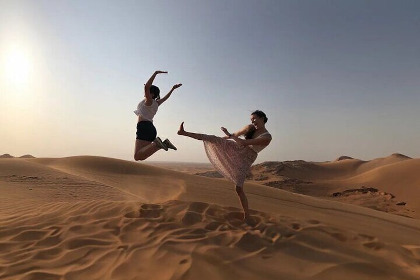 Two people jumping in a desert with sand dunes in the background. 2