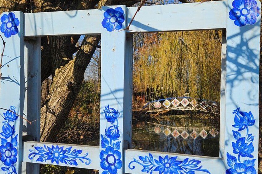 Ein hölzerner Zaun mit blauen floralen Mustern und eine Brücke, die sich im Wasser spiegelt. 3