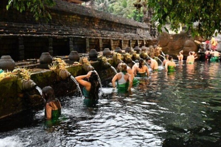 Personas bañándose en un canal de agua con escalones de piedra y una estructura tradicional al fondo. 5