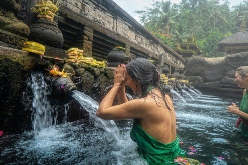 Una persona con un atuendo verde junto a una fuente de agua con una estructura de piedra y un puente al fondo. 4