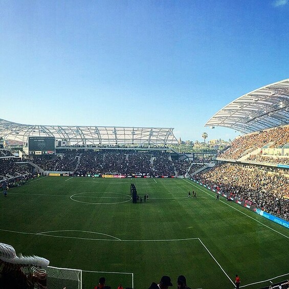 A large stadium with a green field, a goalpost, and a crowd of spectators. 2