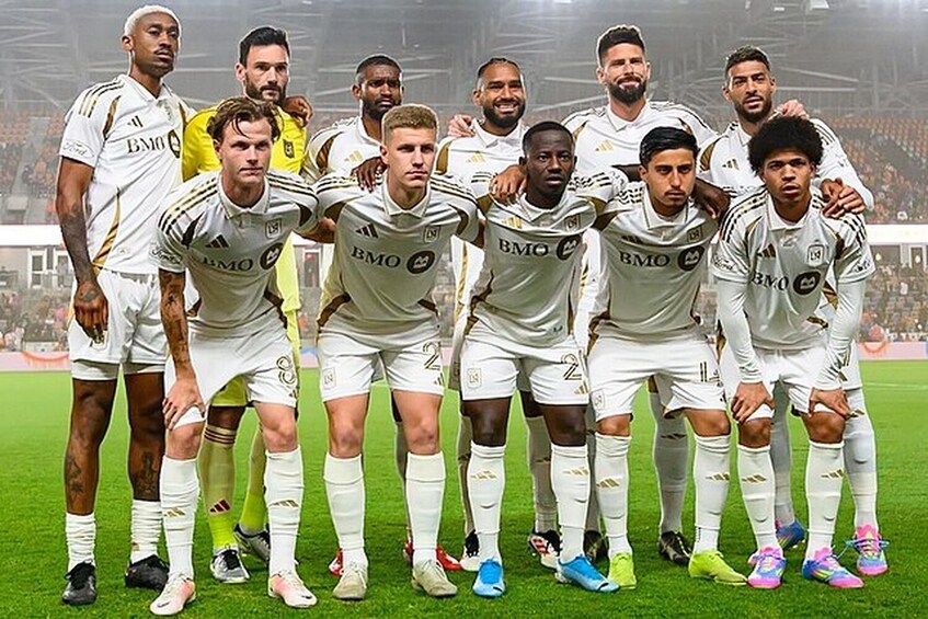 A group of soccer players in white jerseys with 'BMO' on the front, standing on a grassy field. 3