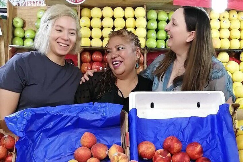 Three people standing in front of a fruit stand with apples and lemons. 2