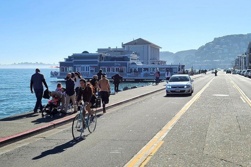 A coastal road with people walking, a cyclist, and a car. 5