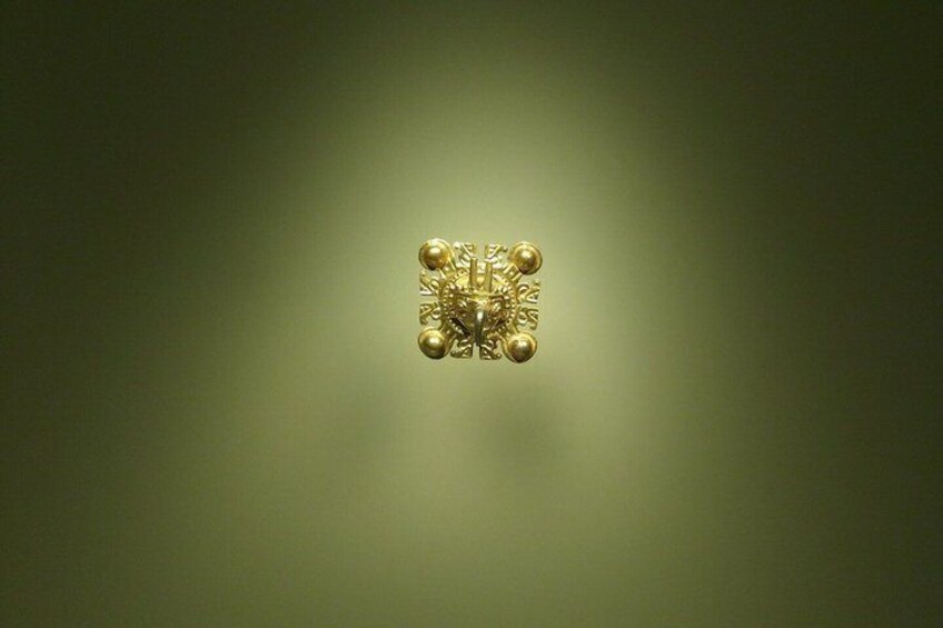 A gold-colored, ornate object with a symmetrical design, centered against a blurred green background. 5