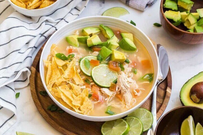 A bowl of soup with tortilla chips, avocado, and lime. 5
