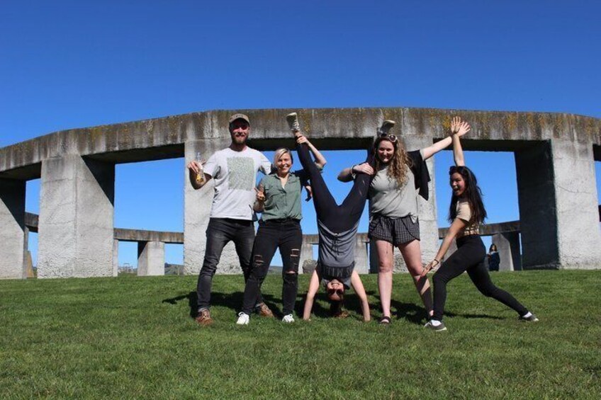 A group of people posing in front of a large concrete structure with grass in the foreground. 4