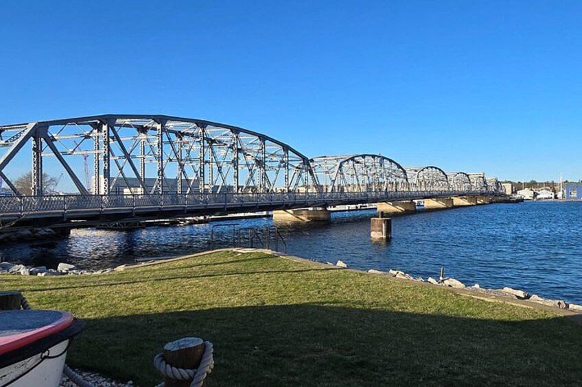 Een stalen brug over een rivier met grasoevers en een boot op de voorgrond. 5