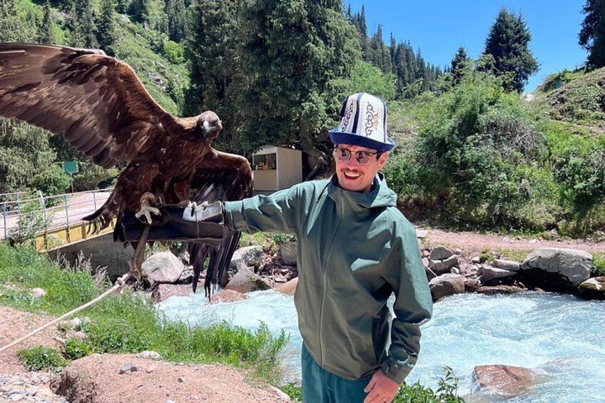 A person wearing a hat and gloves interacting with a large bird of prey near a river. 2