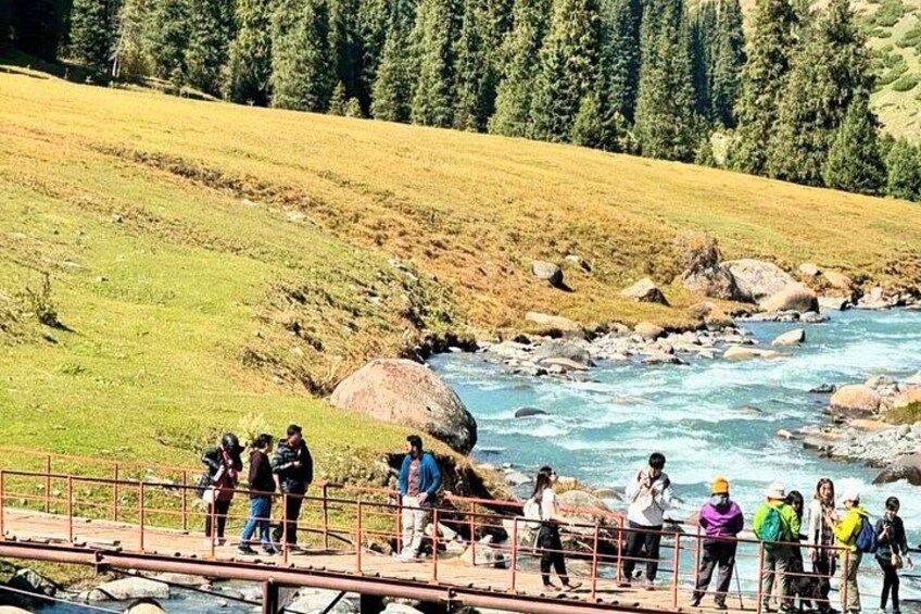 A group of people on a bridge over a river with a forested hillside in the background. 5