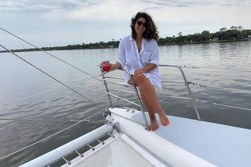 A person sitting on a boat's railing, holding a red object, with calm water and a distant shoreline in the background. 4