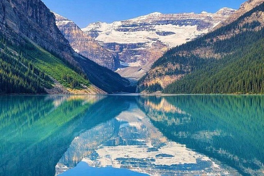 Un lago de montaña con aguas turquesas cristalinas, rodeado de laderas boscosas y montañas nevadas al fondo. 3