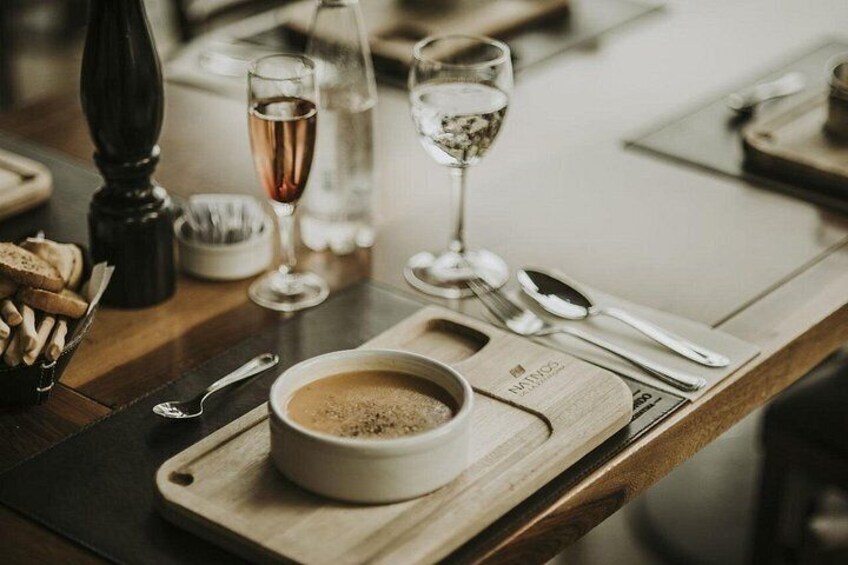 A wooden serving tray with a bowl of soup, a glass of water, and a glass of wine on a table. 4