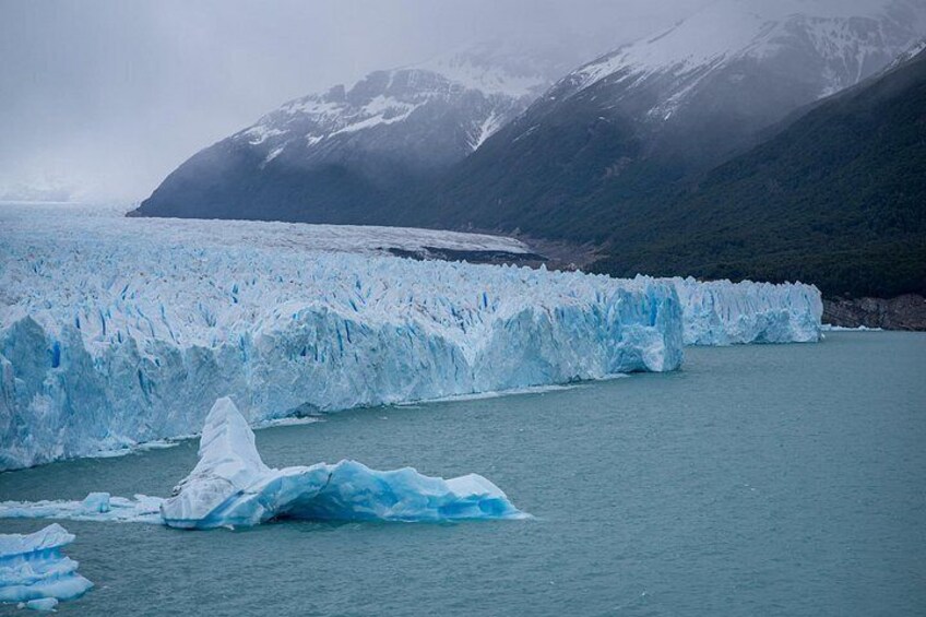 A glacier with icebergs in the water, mountains in the background, and a cloudy sky. 3