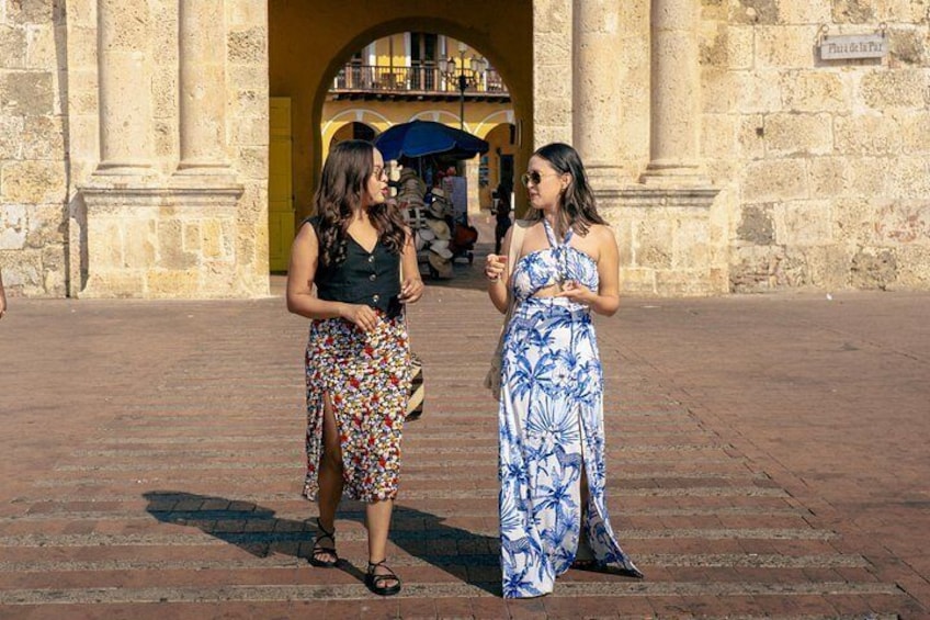 Due donne in piedi in una piazza, con un edificio in pietra sullo sfondo. 3